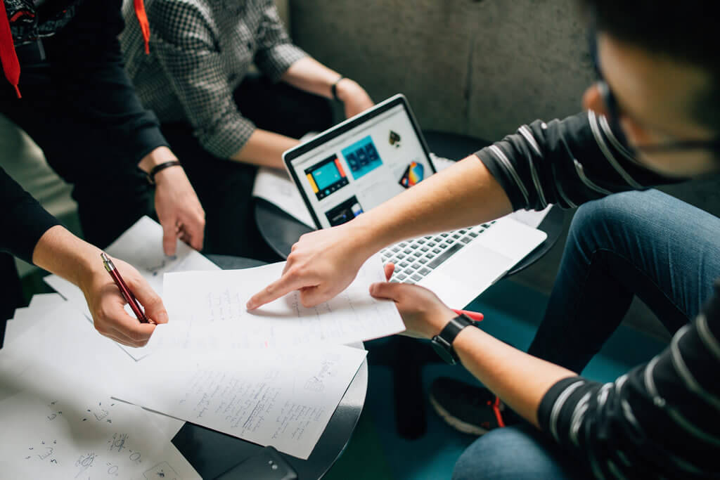 Team planning a project around a table with sketches and a laptop